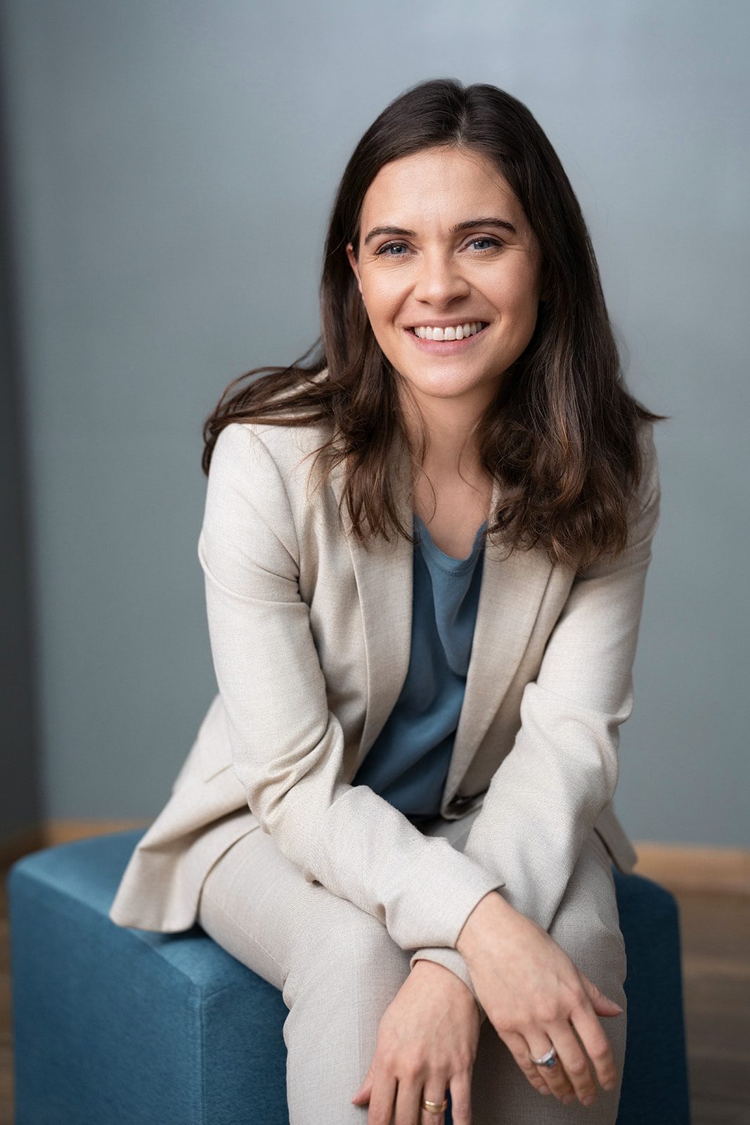 Lächelnde sympathische Frau in beigen Anzug sitzt auf einem Cube